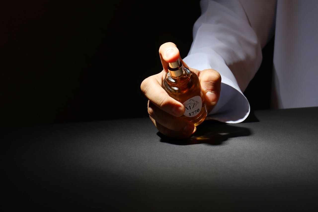 A dramatic close-up of a hand holding a perfume bottle against a dark background, highlighting elegant design.
