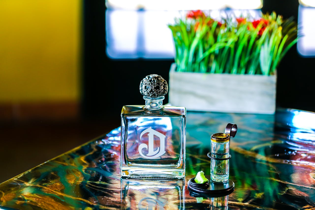 Close-up of a luxurious perfume bottle with a decorative cap on a colorful table with plants in the background.