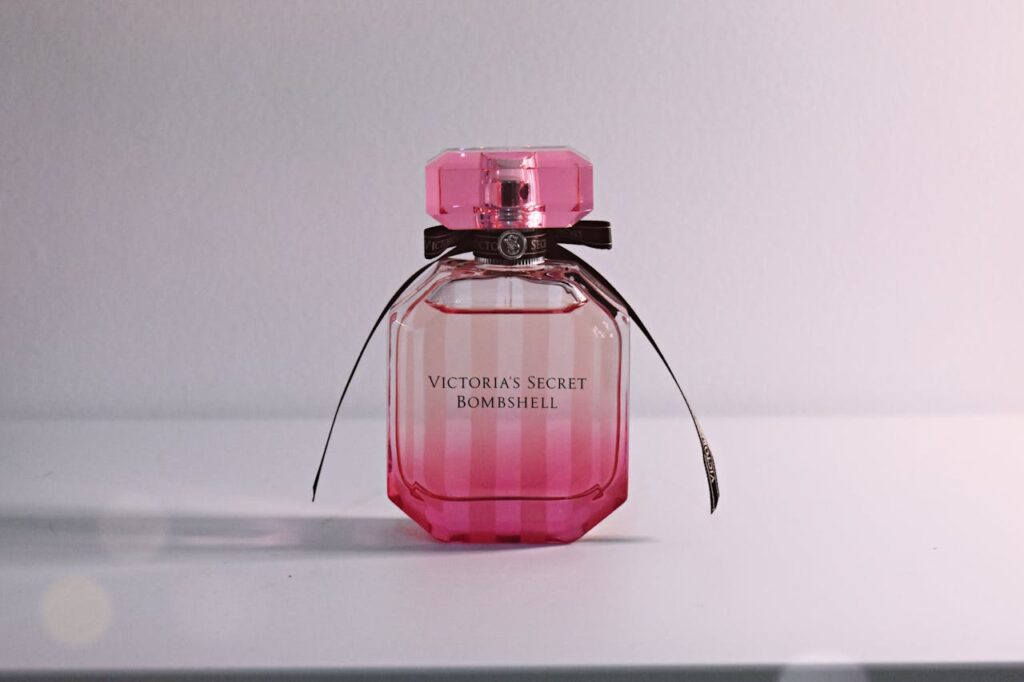 Stylish pink perfume bottle with bow and intricate cap on a white surface.
